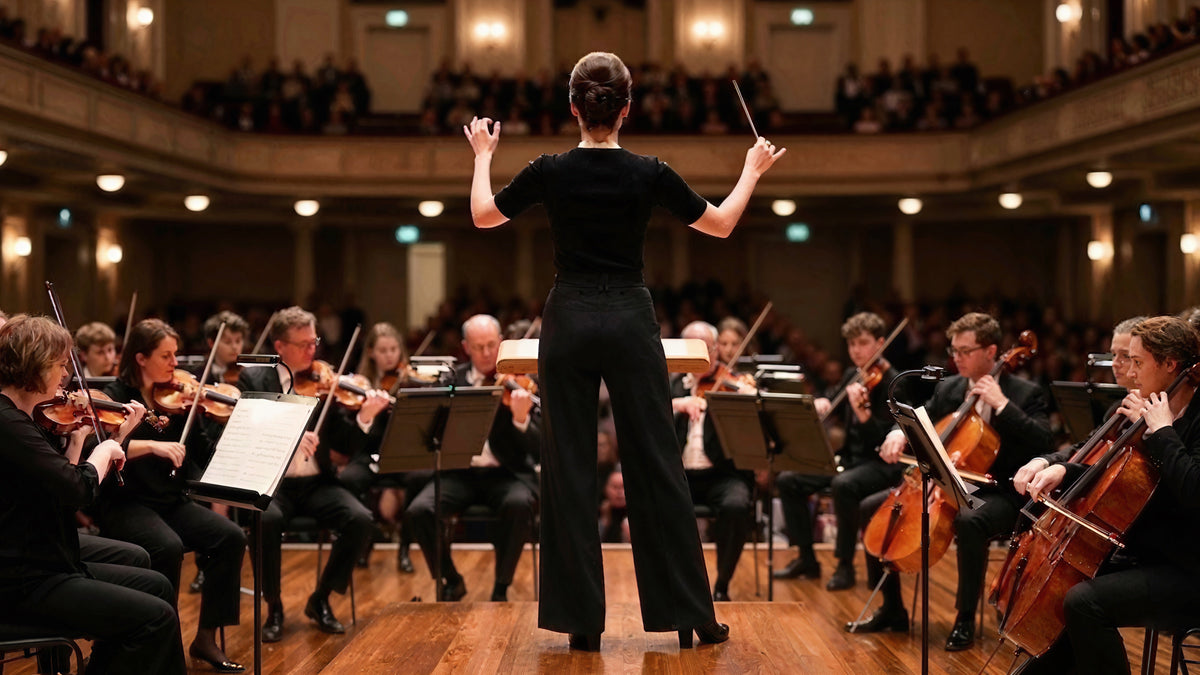 Woman conducting an orchestra in black wide-leg pants, seen from behind