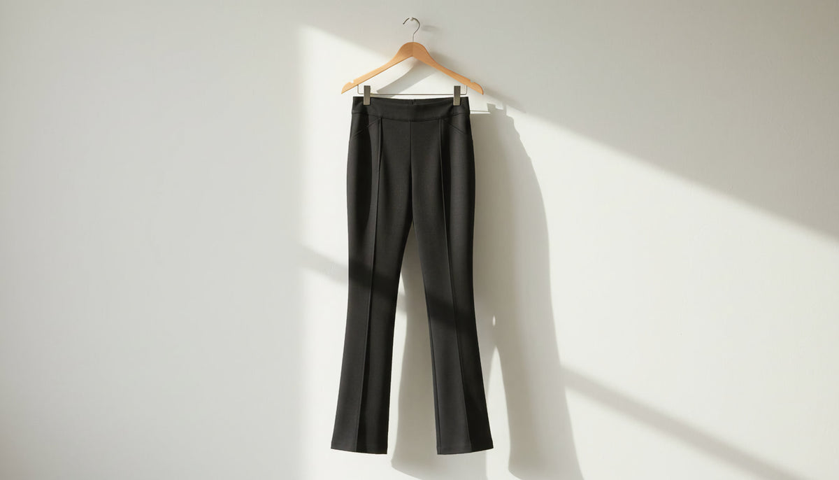 Black ponte pants hanging on a wooden hanger against a sunlit wall