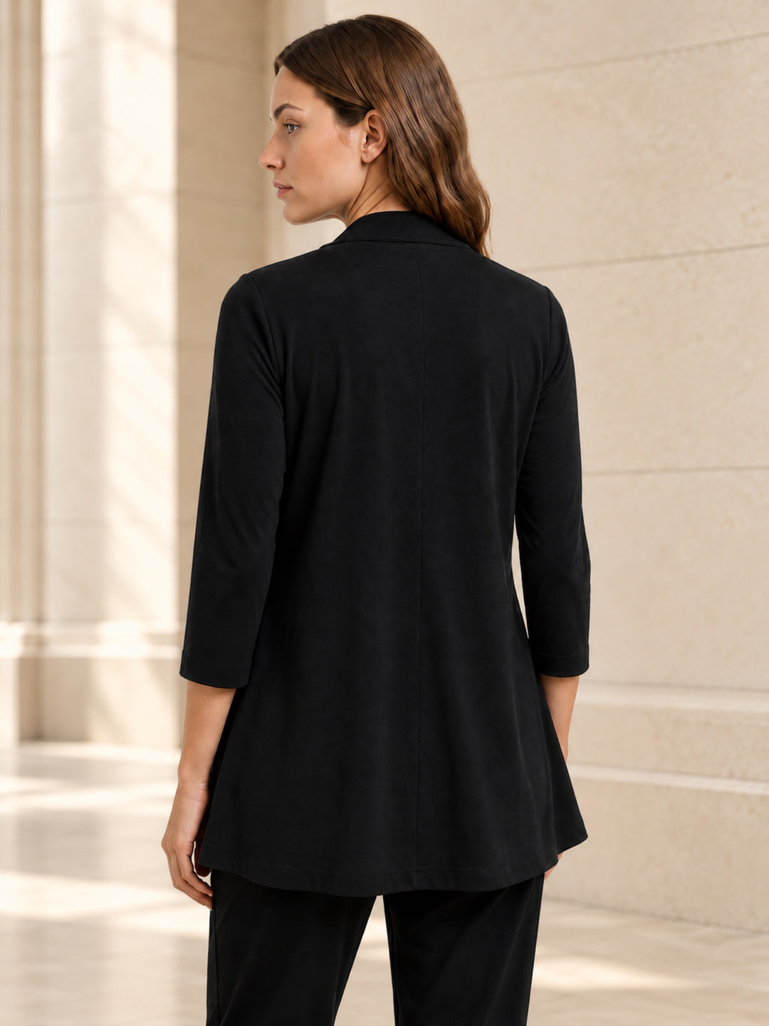 Back view of the Clinton black matte jersey jacket showing its shaped seams and bracelet sleeves in a limestone interior
