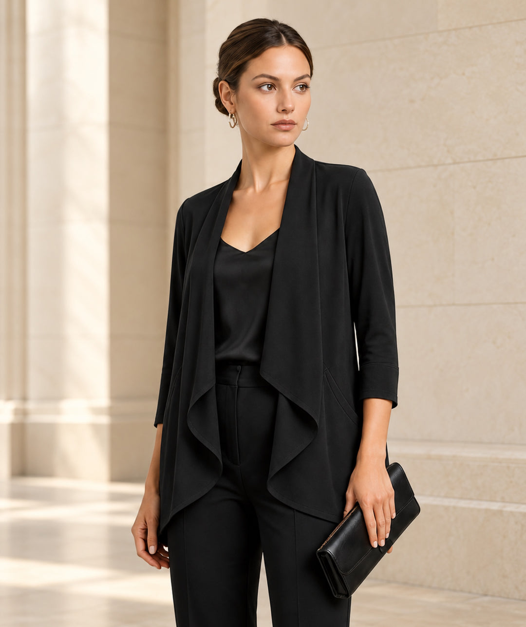The Clinton black open-front jersey jacket styled with a black top and clutch in a softly lit limestone interior